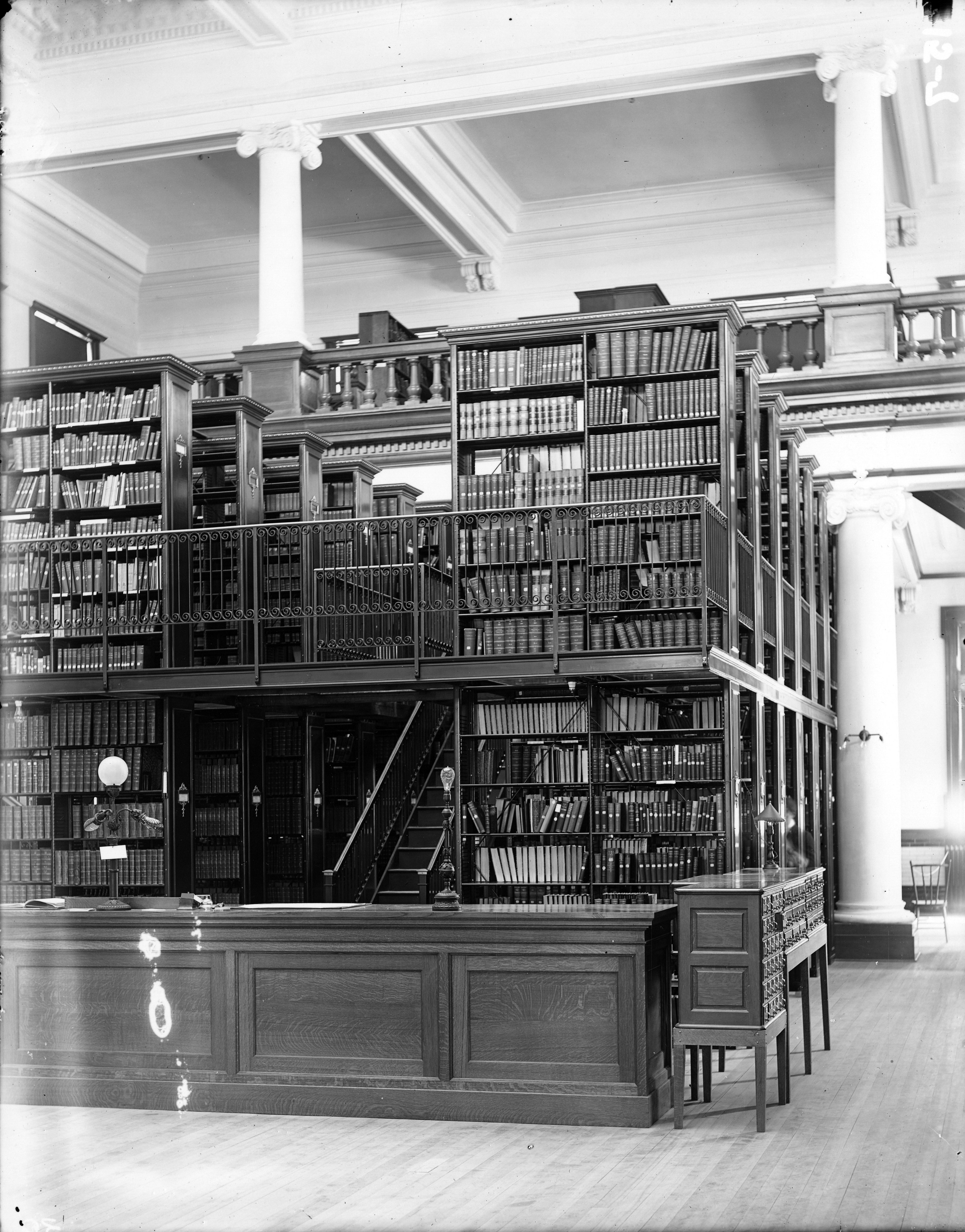 Wielopiętrowe regały biblioteczne z 1904 roku wypełnione tomami — obraz nauki mierzonej ilością, nie wartością: pogoni za punktami i biurokracją.